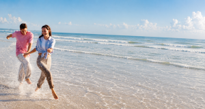 A couple runs along the shoreline at the beach, splashing water and smiling.